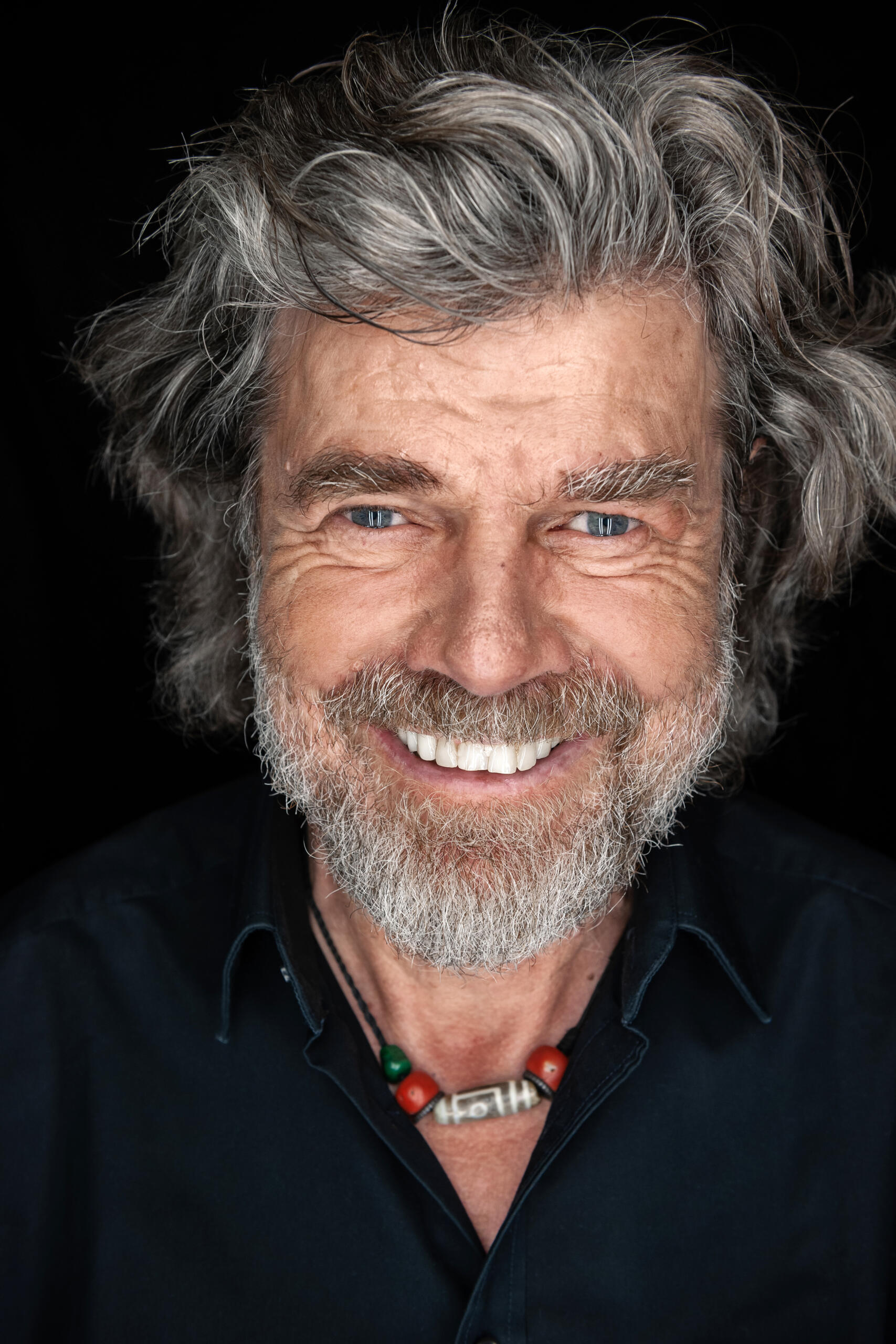 Porträt des Extrembergsteigers und Abenteurers Reinhold Messner, der mit wilden grauen Haaren und graublauen Augen direkt in die Kamera guckt.