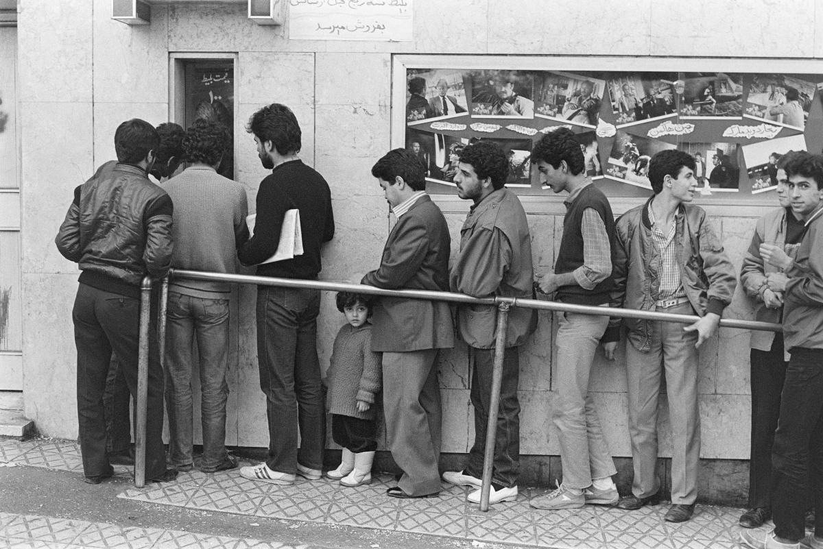 Black and white photograph of some men and a little girl standing in a queue in front of a closed door.