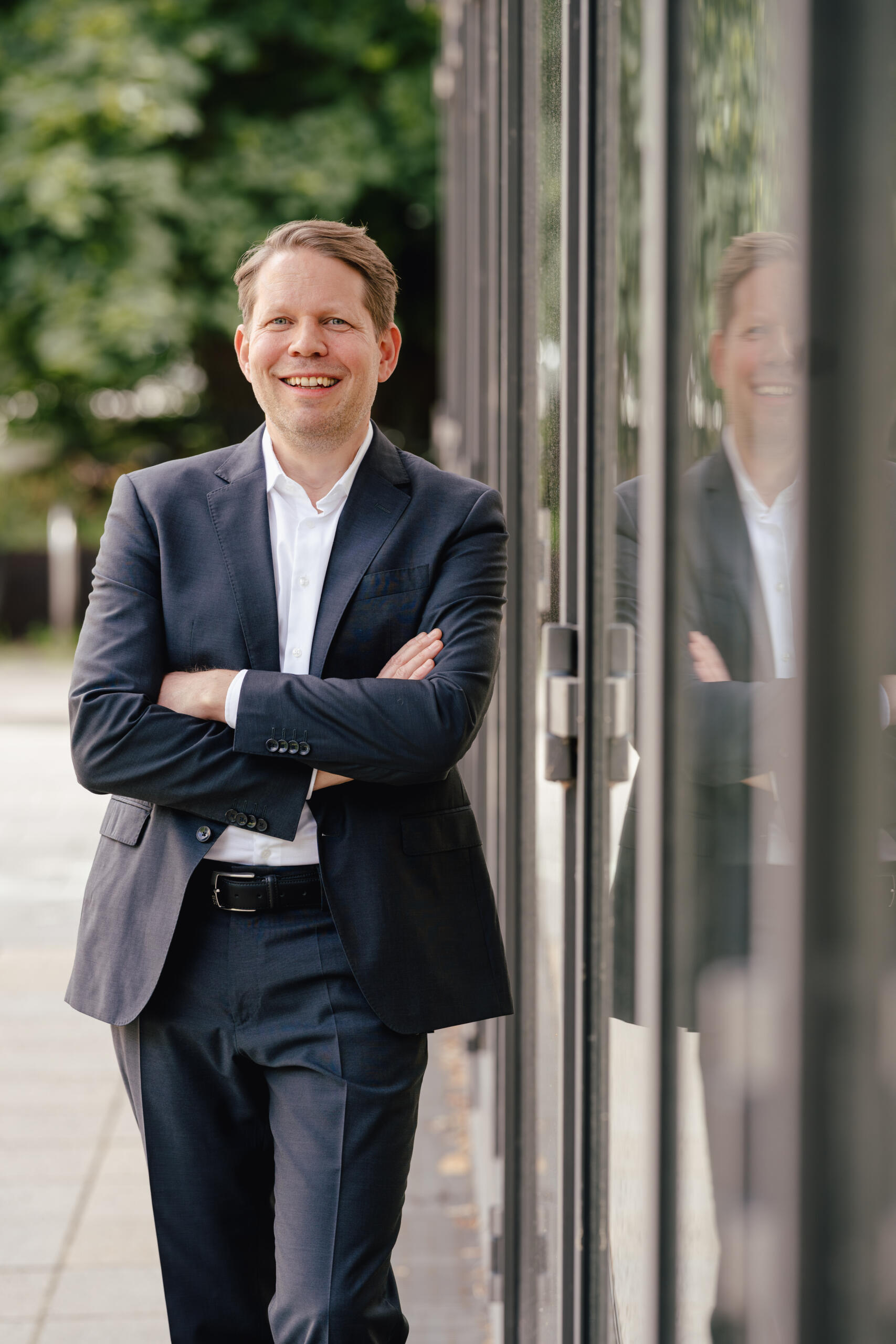 Florian Wiegand leans against a glass façade with his arms crossed.