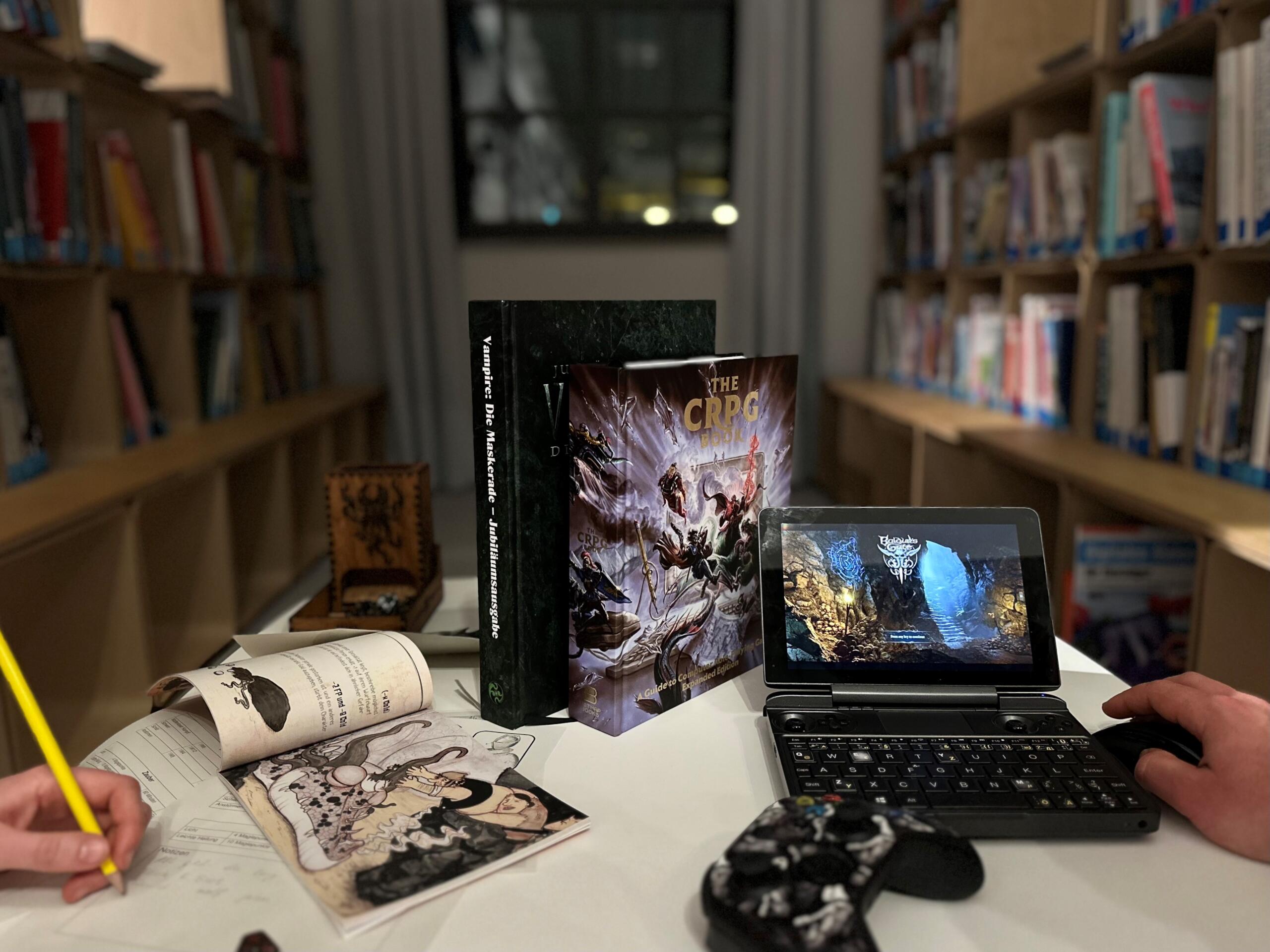 Ein Computer, ein Joypad und Bücher liegen auf einem Tisch.