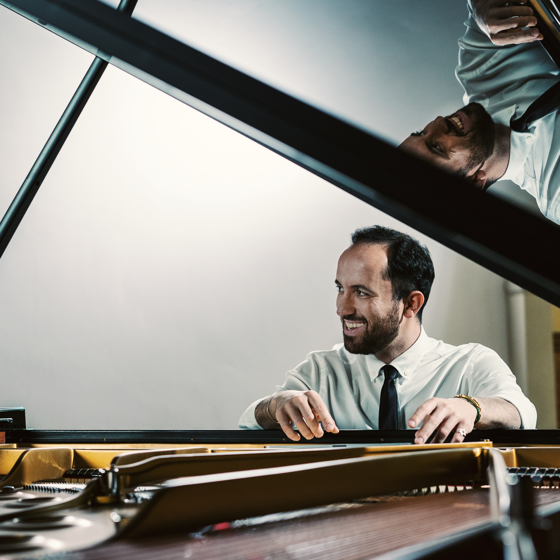 Porträt des Pianisten Igor Levit. Er sitzt in Hemd und Krawatte vor einem aufgeklappten Flügel und lächelt.