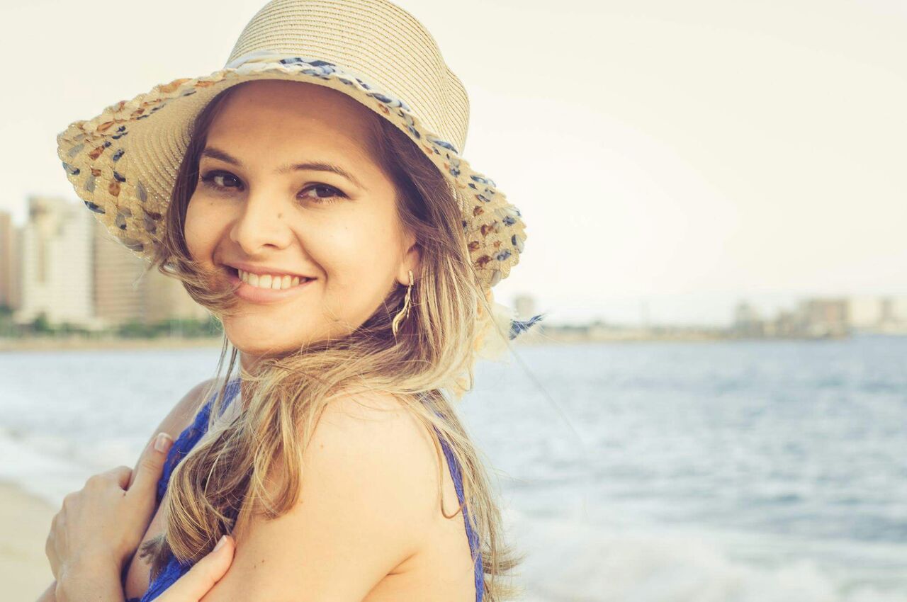 Summer portrait of Joelma Marques on the beach, wearing a straw hat.