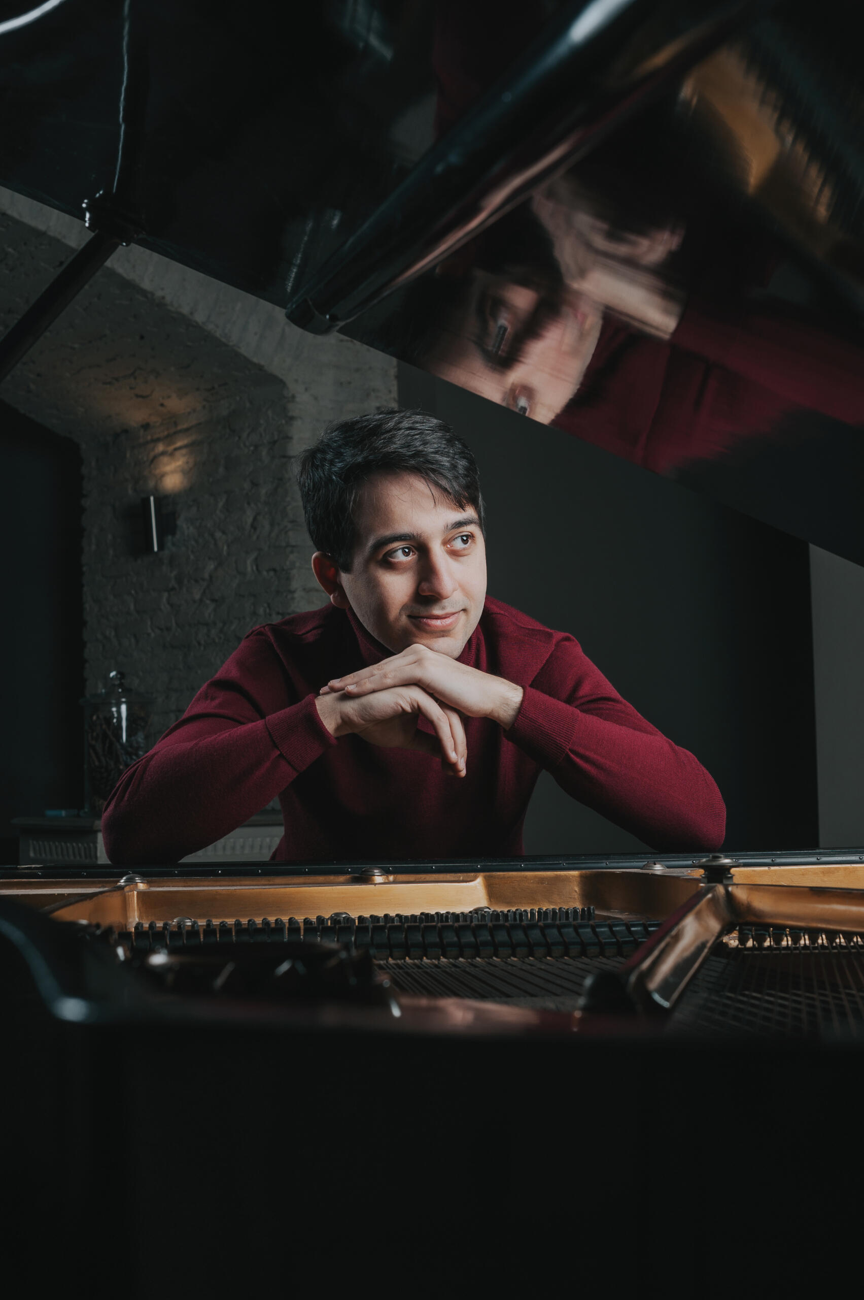 Close-up: Luca Okros sits at the grand piano, smiling pensively and resting his chin on his hands.