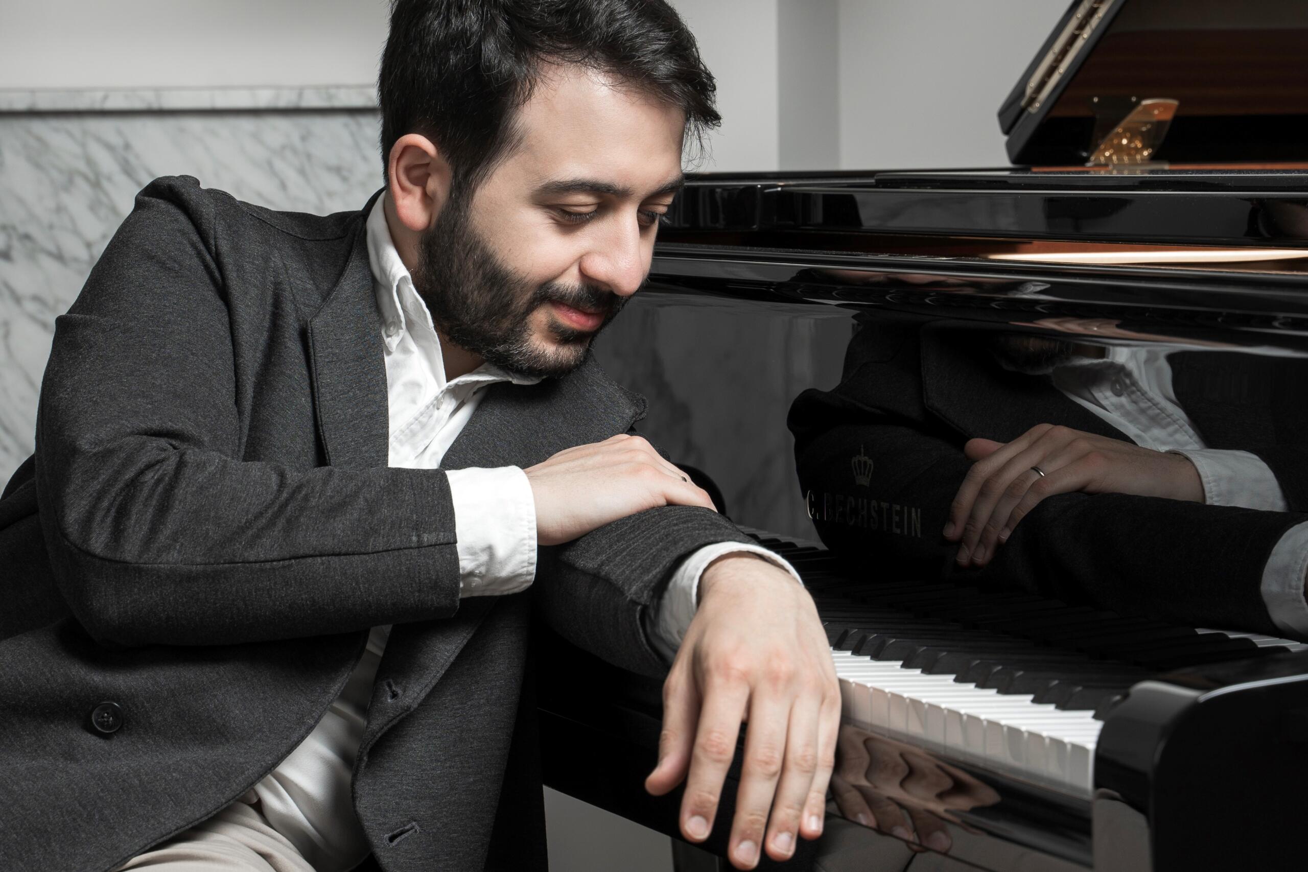 Luka Okros leans on the keyboard of a grand piano.