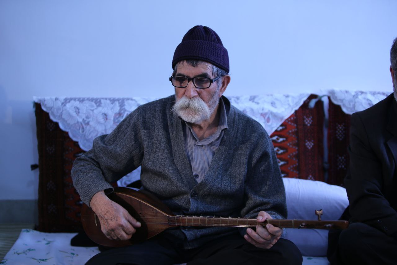 An old man holds a tanbour, a Kurdish plucked instrument, in his hand and plays it.