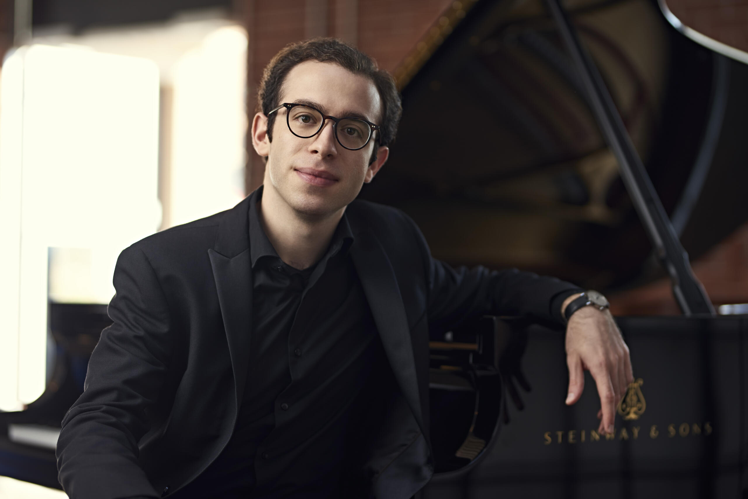 Der Pianist Nicolas Namoradze im Portrait, im Hintergrund ein Flügel.