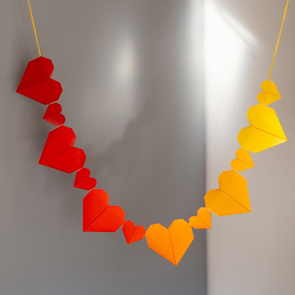 Colourful hearts folded out of paper are strung together to form a chain.