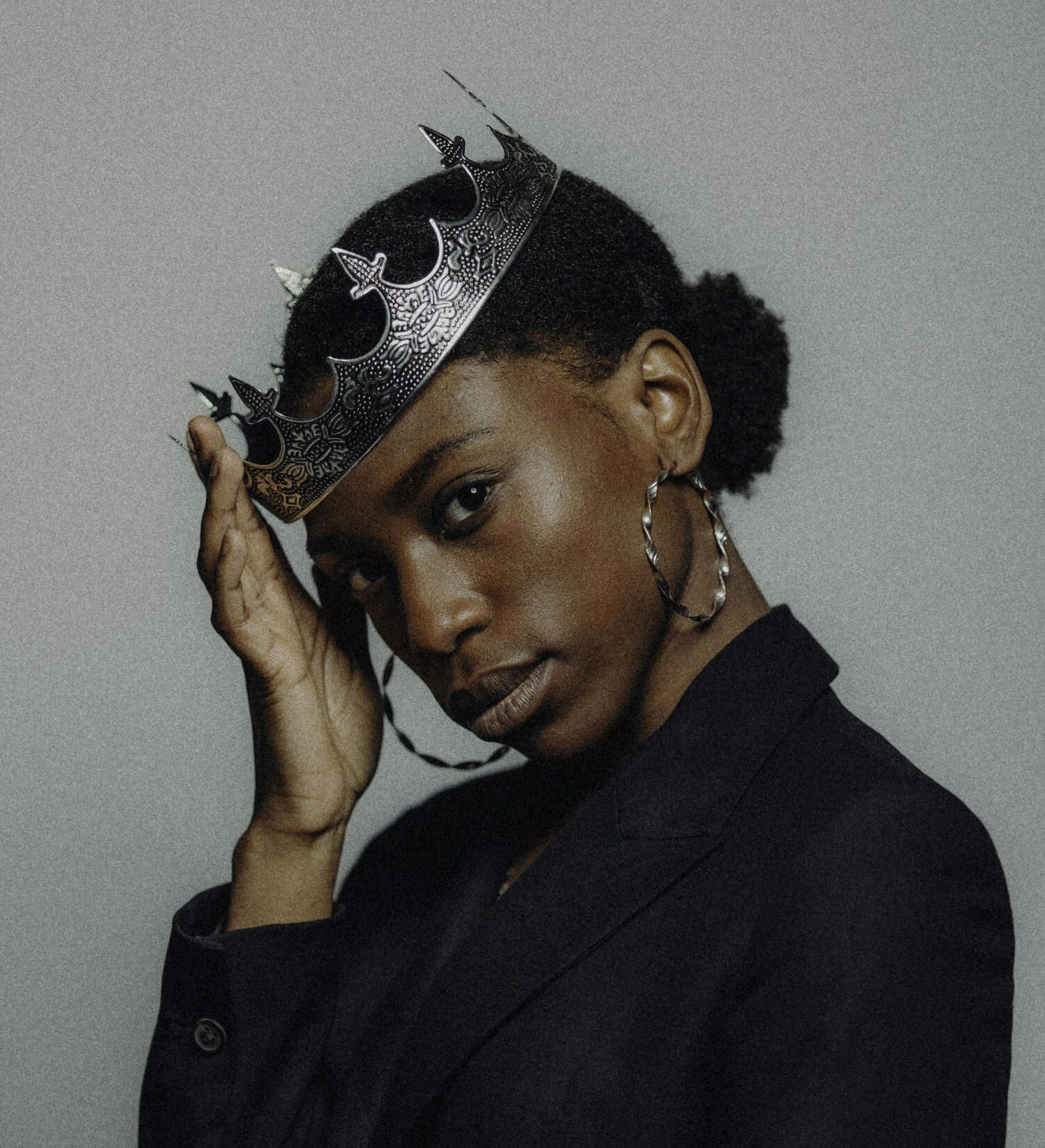 The singer Kokonelle wears a crown and a black blazer and looks directly at the viewer.