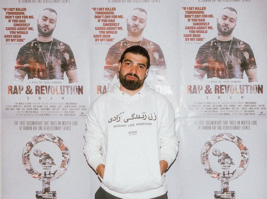 Director Omid Mirnour stands in front of a series of film posters.