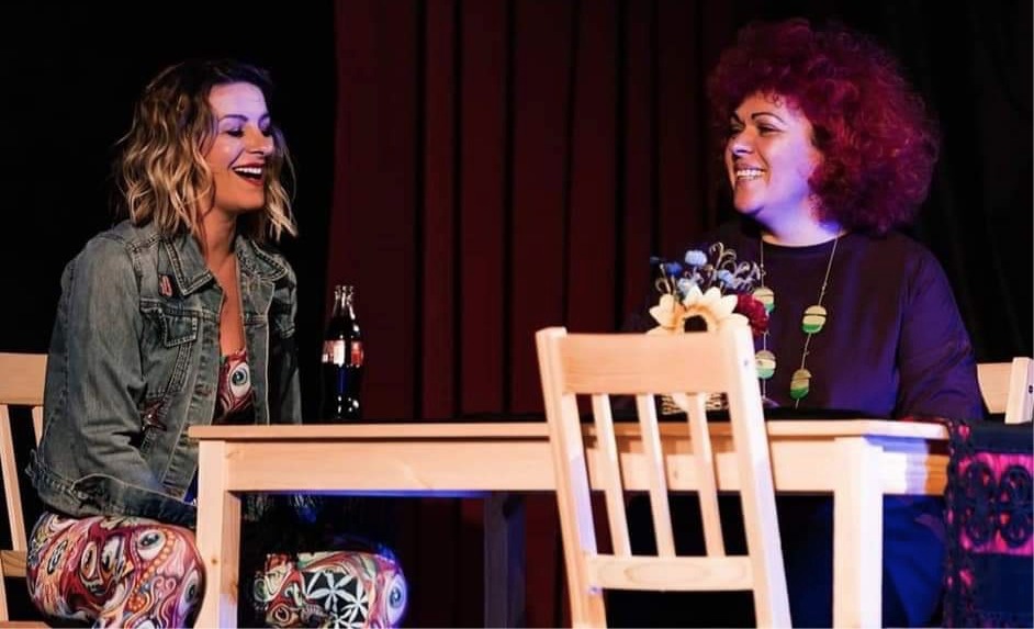 Zwei Frauen sitzen sich an einem Holztisch gegenüber und lächeln sich an.