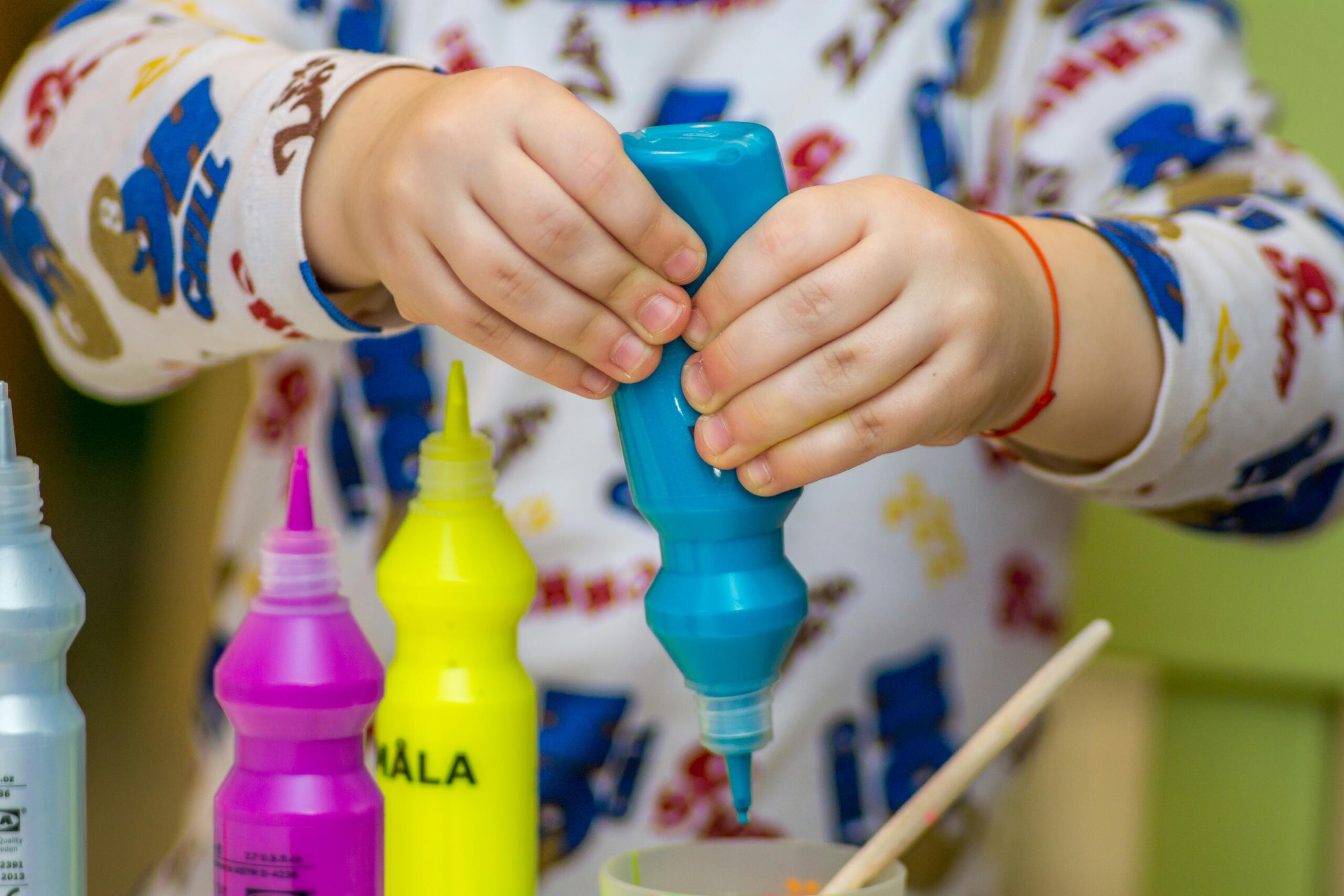 Two children's hands squeeze paint out of a tube.