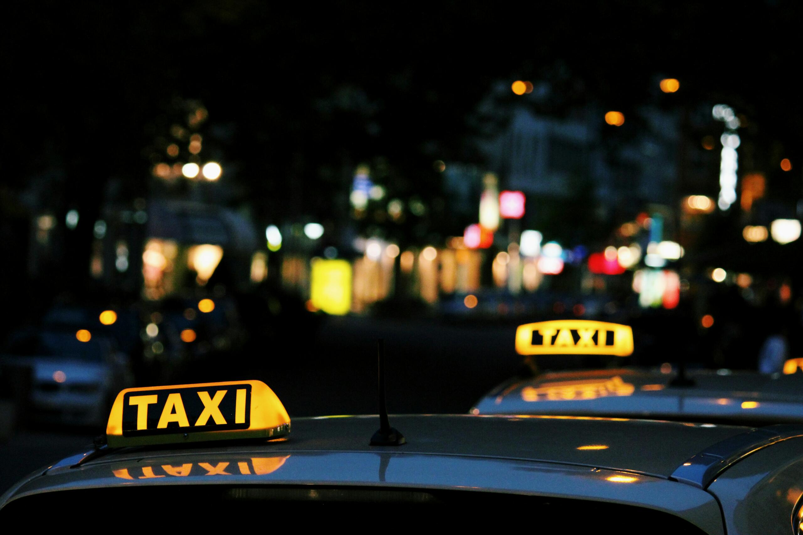 City lights at night, in the foreground the roofs of two taxis with illuminated signs.